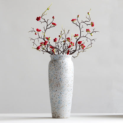 Speckled vase with red floral branches on a light gray background