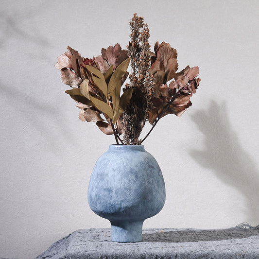 Blue ceramic vase with dried flowers on a textured surface against a light gray background