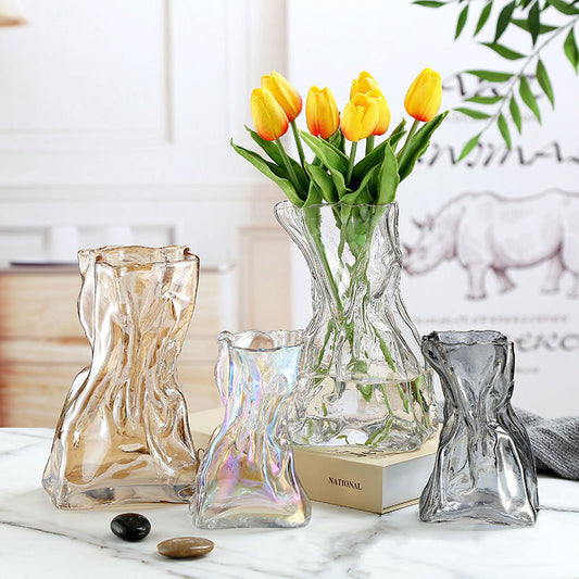 Clear glass vases with unique designs on a marble surface, one containing yellow tulips.