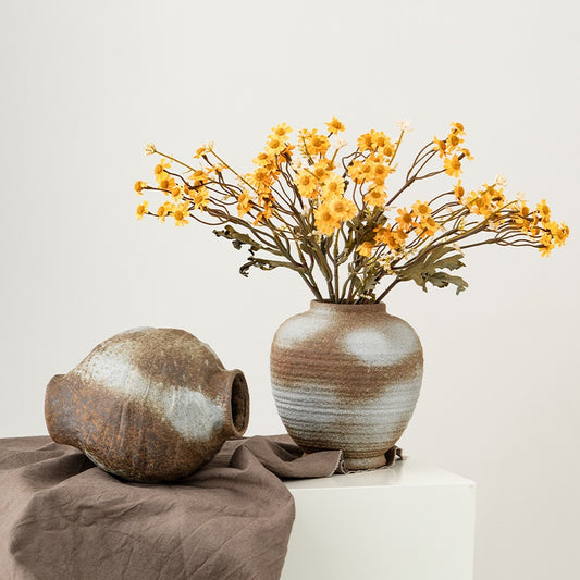 Two ceramic vases with one containing yellow flowers on a neutral background