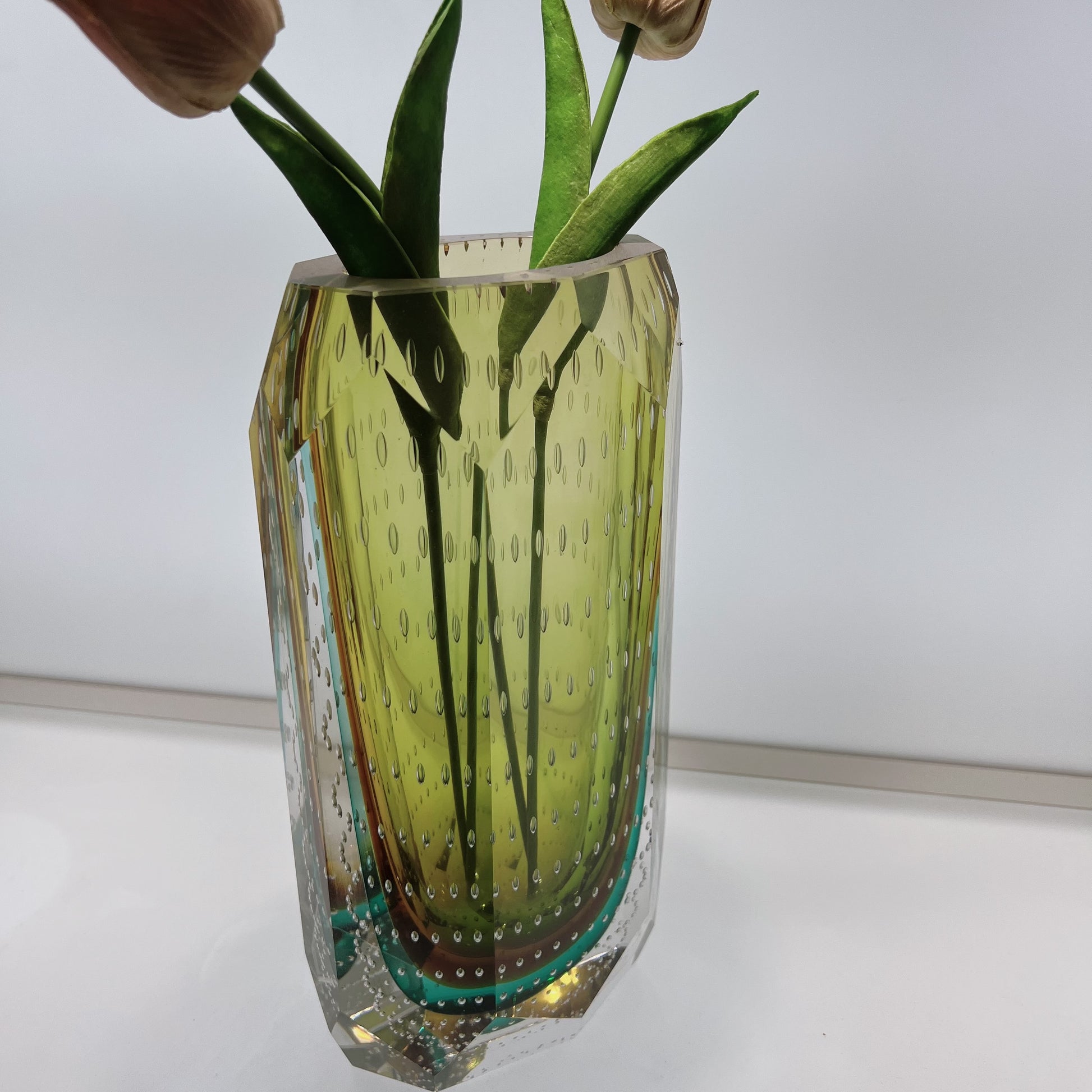 Glass vase with textured design containing green leaves on a white background