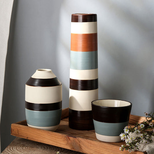 Three ceramic vases with striped design on a wooden shelf against a gray wall.