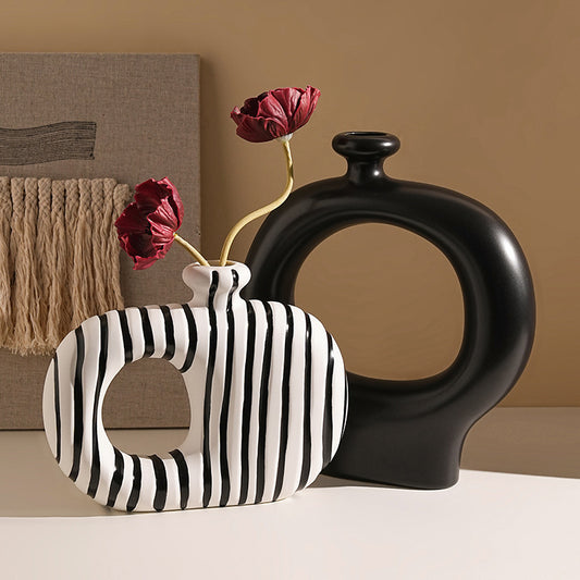 Black and white striped vase with red flowers against a beige wall