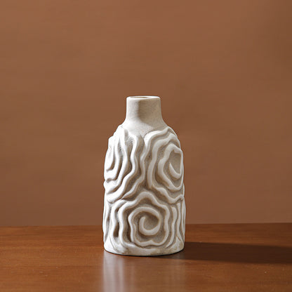 White ceramic vase with wavy patterns on a wooden surface and brown background