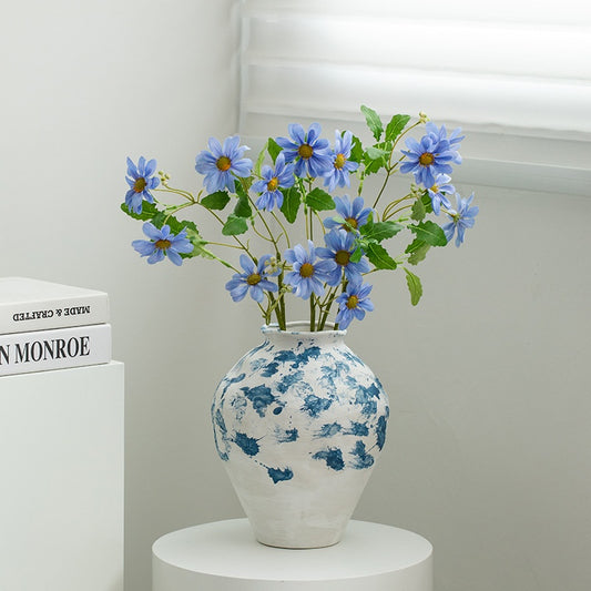 White vase with blue floral patterns holding blue flowers on a white surface.
