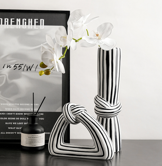 Black and white striped vase with a candle and framed picture on a table