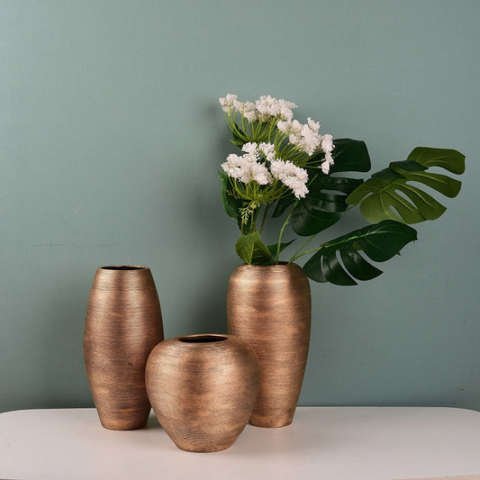 Three bronze vases on a white surface with a green wall background