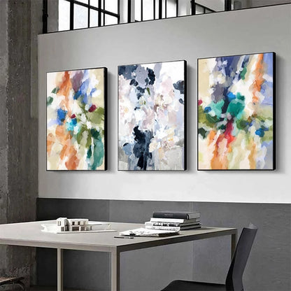 Three abstract art pieces on a wall above a desk.