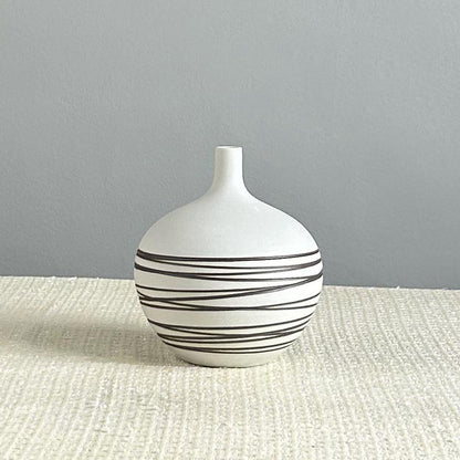 White vase with black stripes on a textured surface and gray background