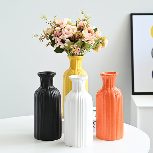 Four vases in black, white, yellow, and orange on a table with a bouquet of flowers.