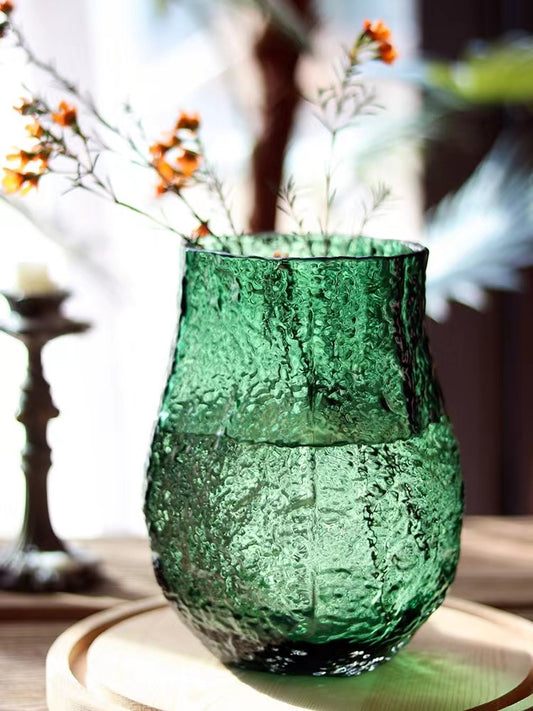 Green textured glass vase with dried flowers on a blurred background