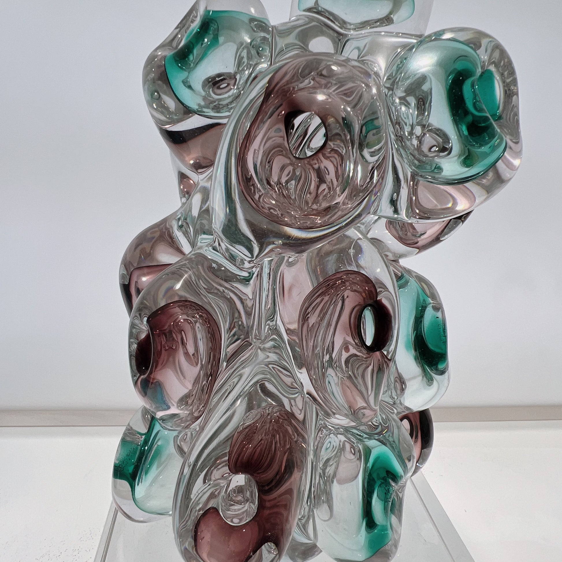 Glass sculpture with swirl patterns in green, brown, and clear on a white background