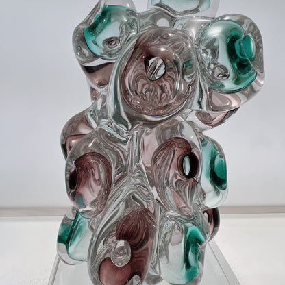 Glass sculpture with swirl patterns in green, brown, and clear on a white background