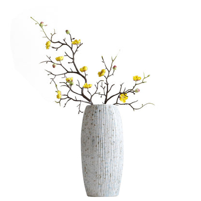Decorative vase with textured surface holding branches with yellow flowers on a white background
