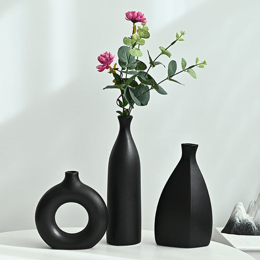 Three black vases on a white surface with a branch of pink flowers and green leaves.