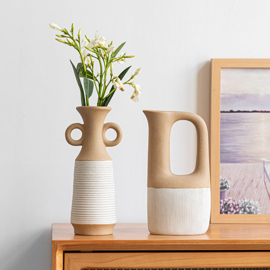 Two ceramic vases on a wooden surface with a framed picture in the background.