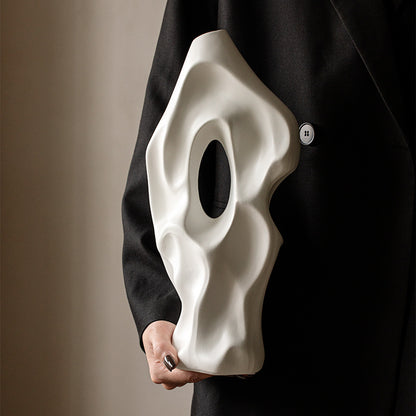 Person holding a white mask against a black coat on a beige background