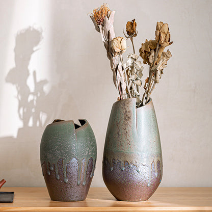 Two ceramic vases with textured finish on a wooden surface, one containing dried flowers.