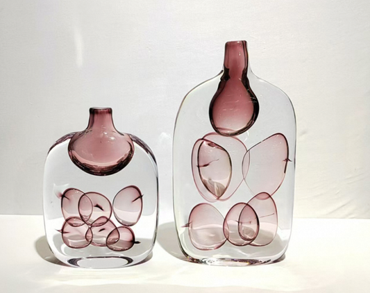 Two glass vases with pink interior and abstract design on a white background