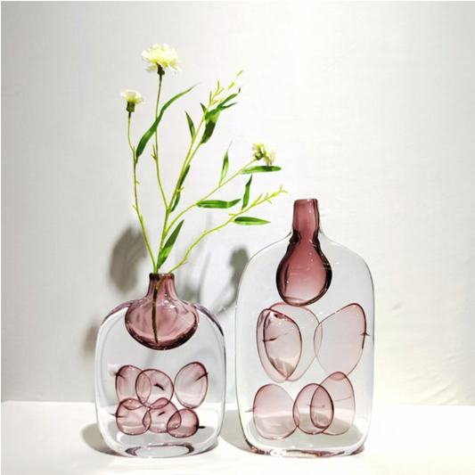 Two glass vases with pink butterfly designs and a plant on a white background