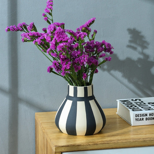 Black and white striped vase with purple flowers on a wooden surface against a gray wall.