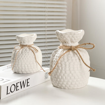 Two white textured ceramic pots with twine on a surface with a LOEWE book in the background.