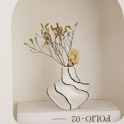 White vase with blue stripes holding dried flowers on a white surface with 'Folio-02' branding.