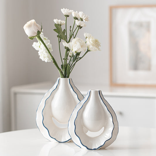 Two white vases with blue rims holding flowers on a table.