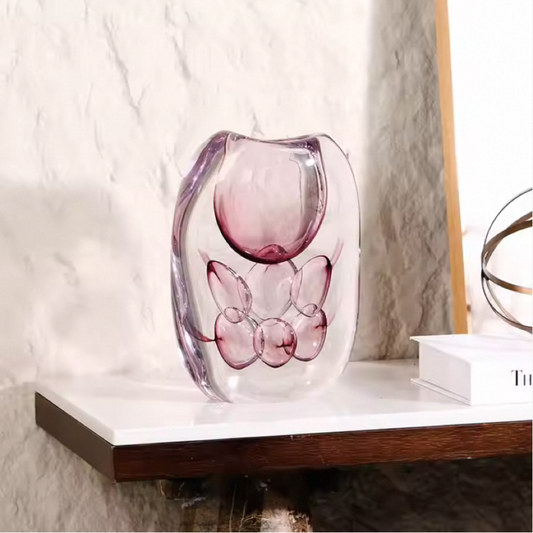 Pink glass sculpture on a white surface with a marble wall background