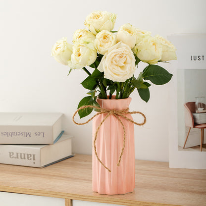 Pink vase with white roses on a wooden surface with books in the background