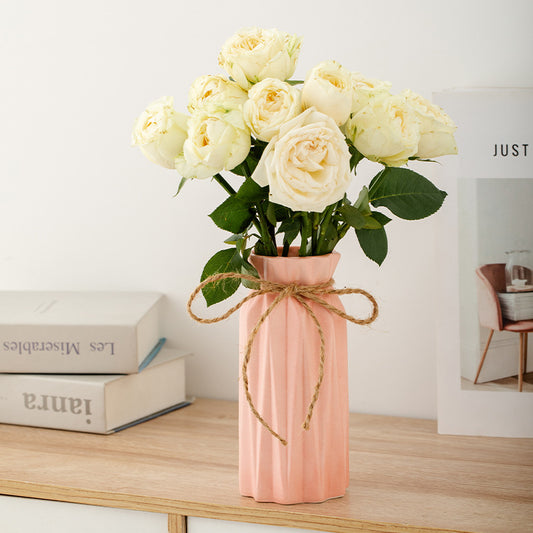 Pink vase with white roses on a wooden surface with books in the background