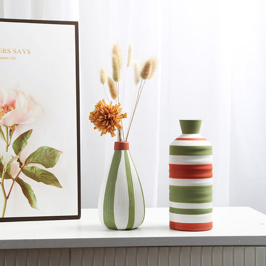 Two decorative vases with striped patterns on a surface, one with dried flowers, against a light background.
