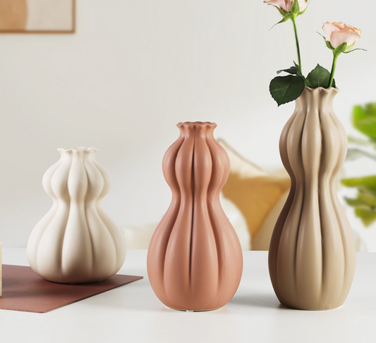 Three ceramic vases of different shapes and colors on a light surface with a neutral background.