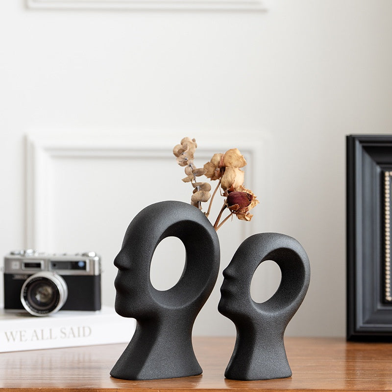Two black ceramic head-shaped vases on a wooden surface with a blurred background.