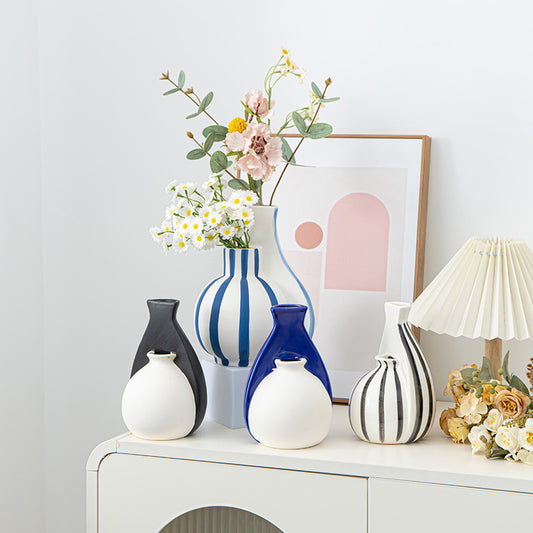Collection of decorative vases and a lamp on a white surface with a light gray wall in the background.