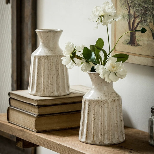 Two ceramic vases on a wooden surface with one containing white flowers.