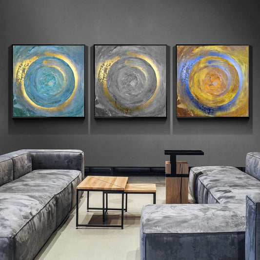 Three abstract paintings on a wall above a gray sofa in a living room.