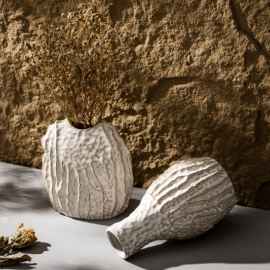 Two textured ceramic vases with dried plants against a stone wall.