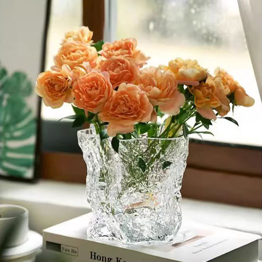 Clear glass vase with peach-colored flowers on a surface with a blurred background