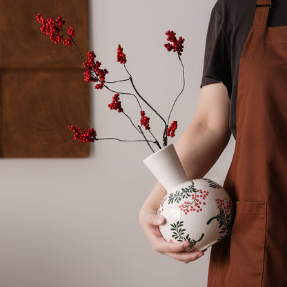 Person holding a white vase with red floral design against a neutral background