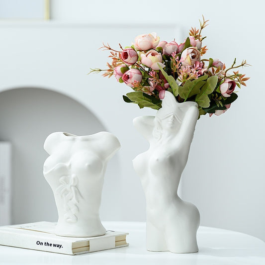 White vase shaped like a torso holding flowers on a white surface with a light gray background