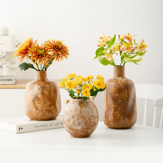 Three rustic-style vases with flowers on a white surface