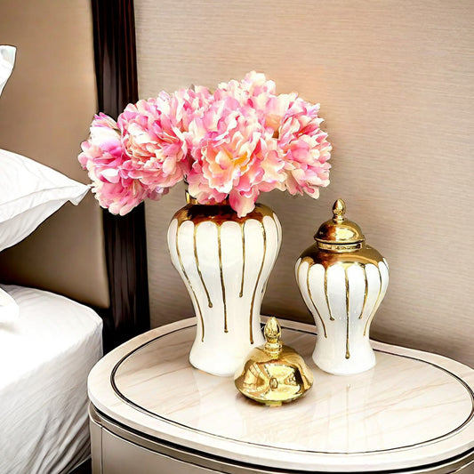 Decorative table with a vase of pink flowers, a gold bell, and a white and gold decorative container.
