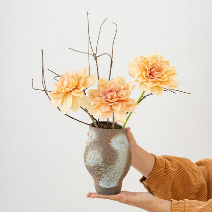 Person holding a vase with peach-colored flowers against a light background