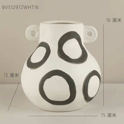 White vase with black circular patterns on a beige background