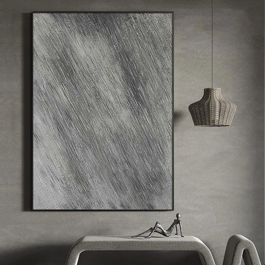 Abstract art piece on a gray wall with a table and lamp below.