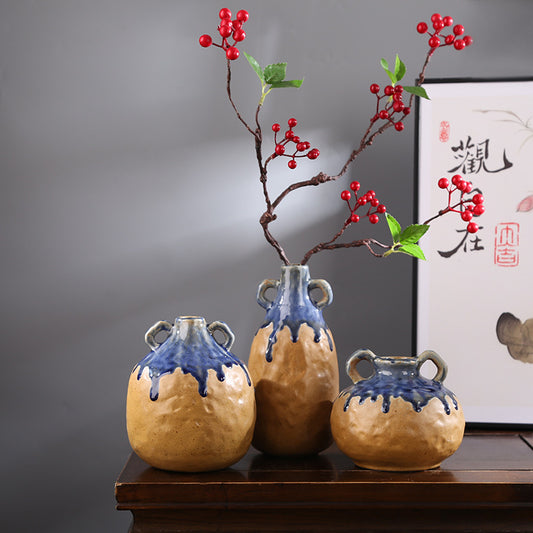Three ceramic vases with blue glaze on a wooden surface, with a framed artwork in the background.