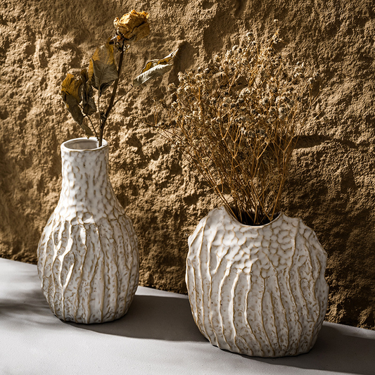 Two textured ceramic vases with dried plants against a stone wall.