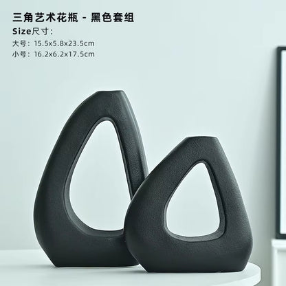 Two black artistic vases on a white surface with a light gray background