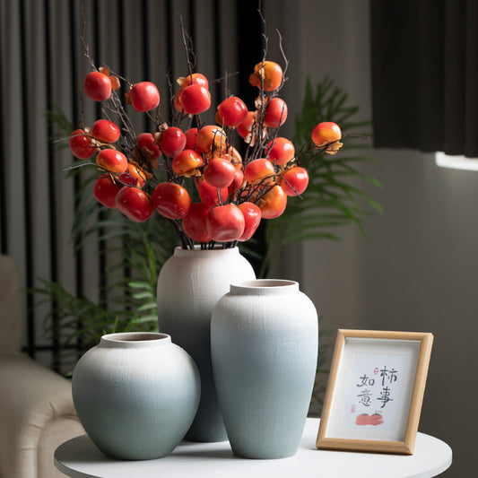 Three ceramic vases with a decorative branch of red and orange fruits on a table.